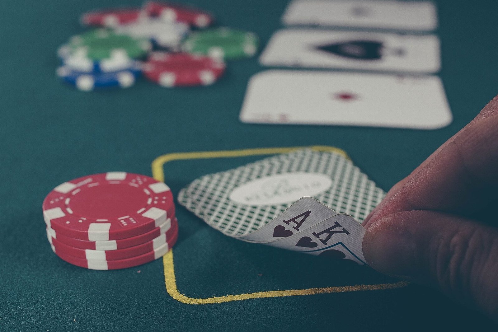 Table de poker au tapis bleu-vert avec une pile de jetons rouges, des cartes retournées et un joueur qui soulève un As et un Roi