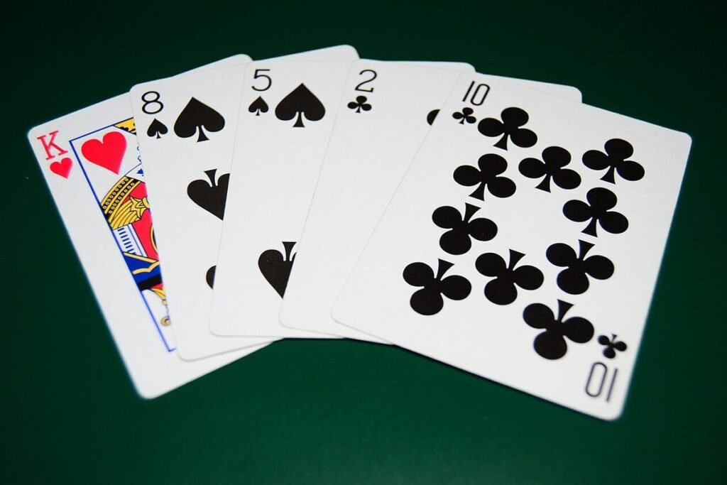Main de poker dépareillée étalée sur un tapis vert : Roi de cœur, 8 et 5 de pique, 2 et 10 de trèfle