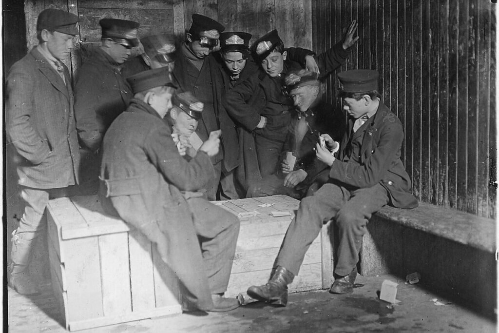 Photographie ancienne en noir et blanc de jeunes coursiers de la Western Union jouant au poker sur une caisse en bois, au début du XXe siècle
