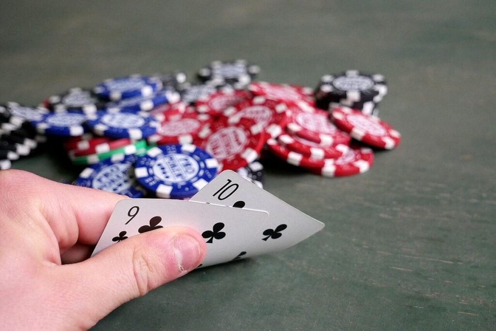 Main d'un joueur soulevant discrètement un 9 et un 10 de trèfle devant un tas de jetons sur le tapis